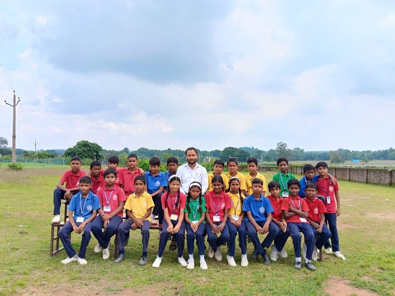 A class of students in house colours seated with their teacher on the school ground