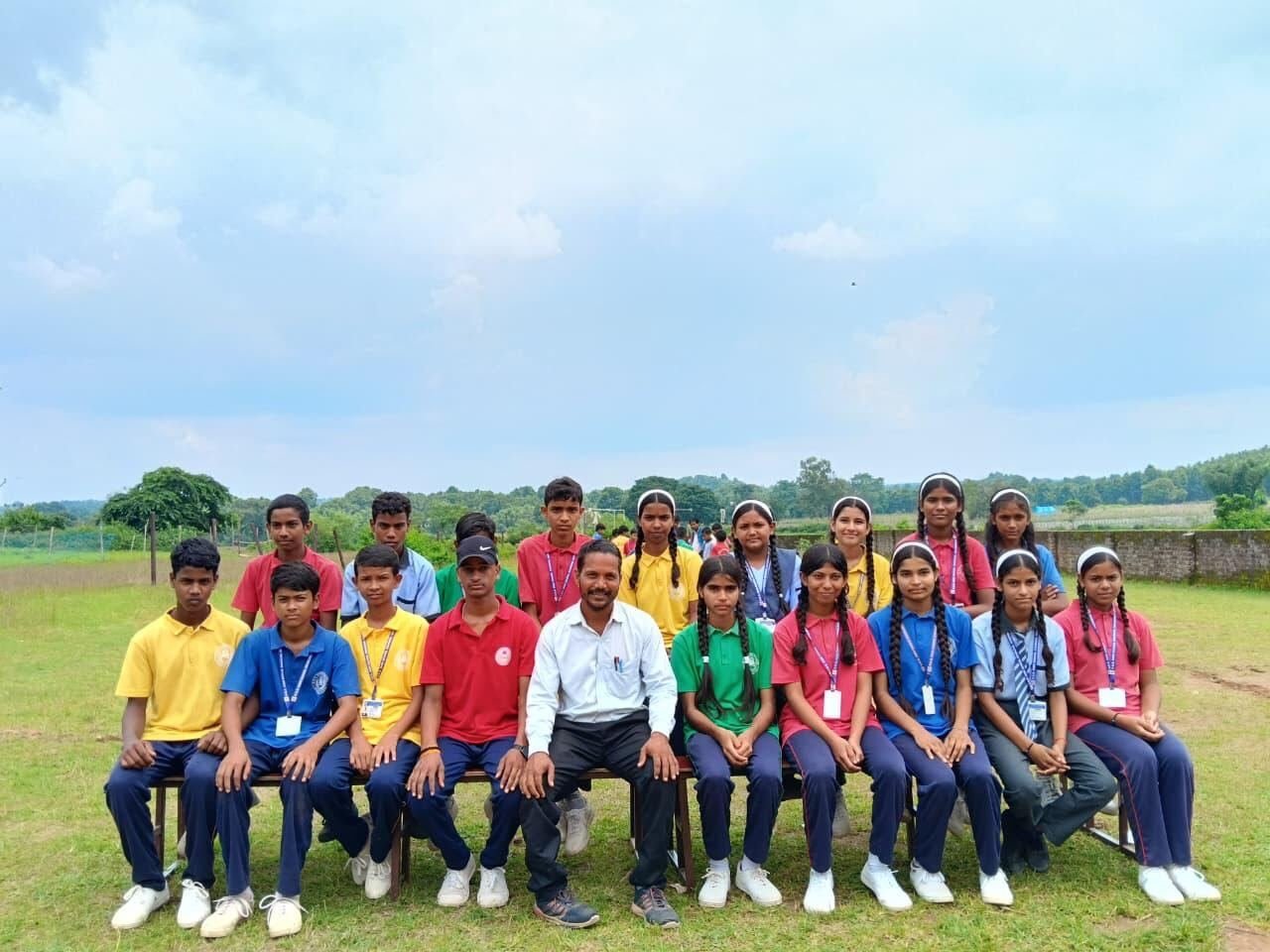 Senior students in house colours seated with a male teacher on the school ground