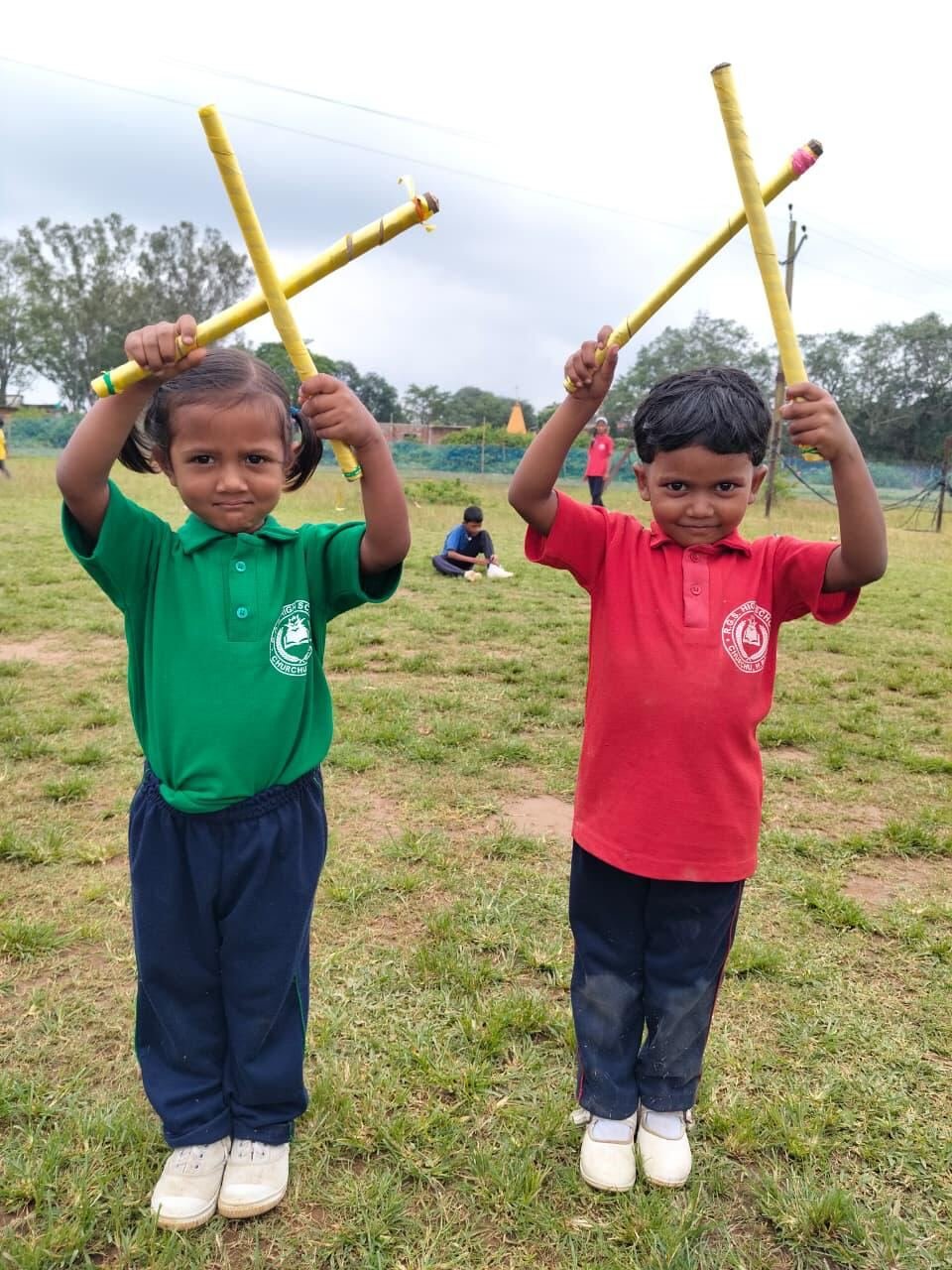Two young RGS pupils smiling and holding up yellow sticks on the field