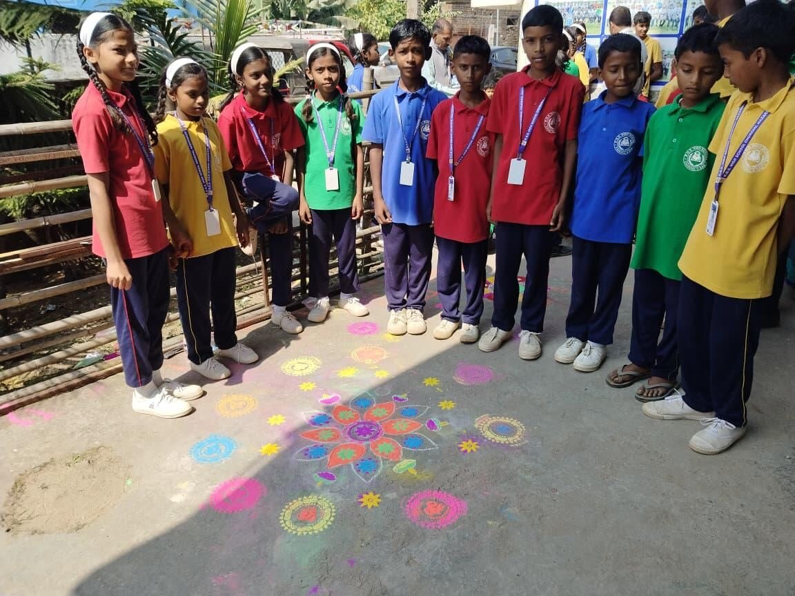 Students standing behind a colourful rangoli drawn at the school entrance