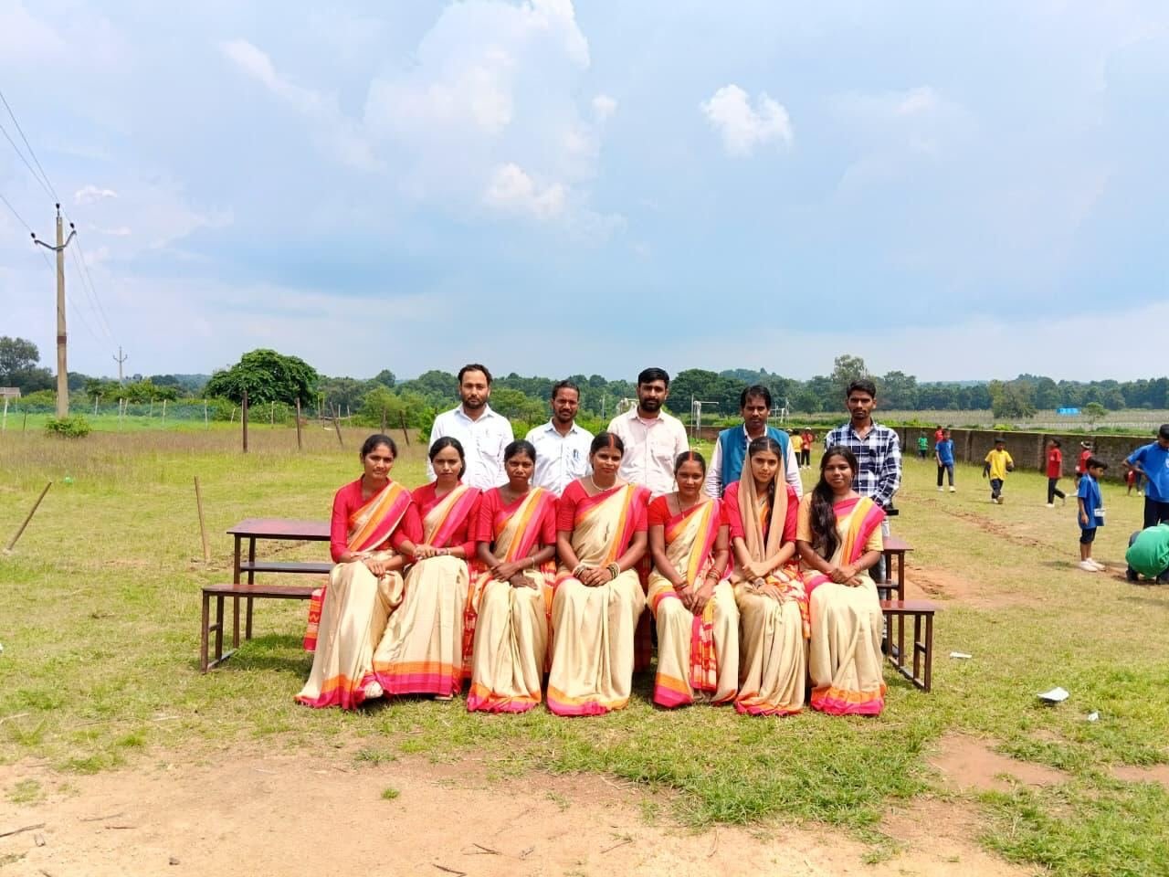 RGS teachers in matching sarees seated in front, with male staff standing behind, on the school ground